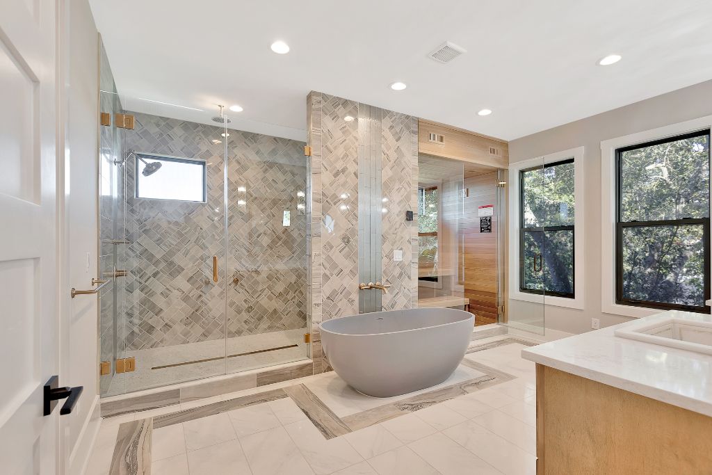 Spa master bathroom with herringbone marble tile, freestanding soaking tub, glass shower and sauna