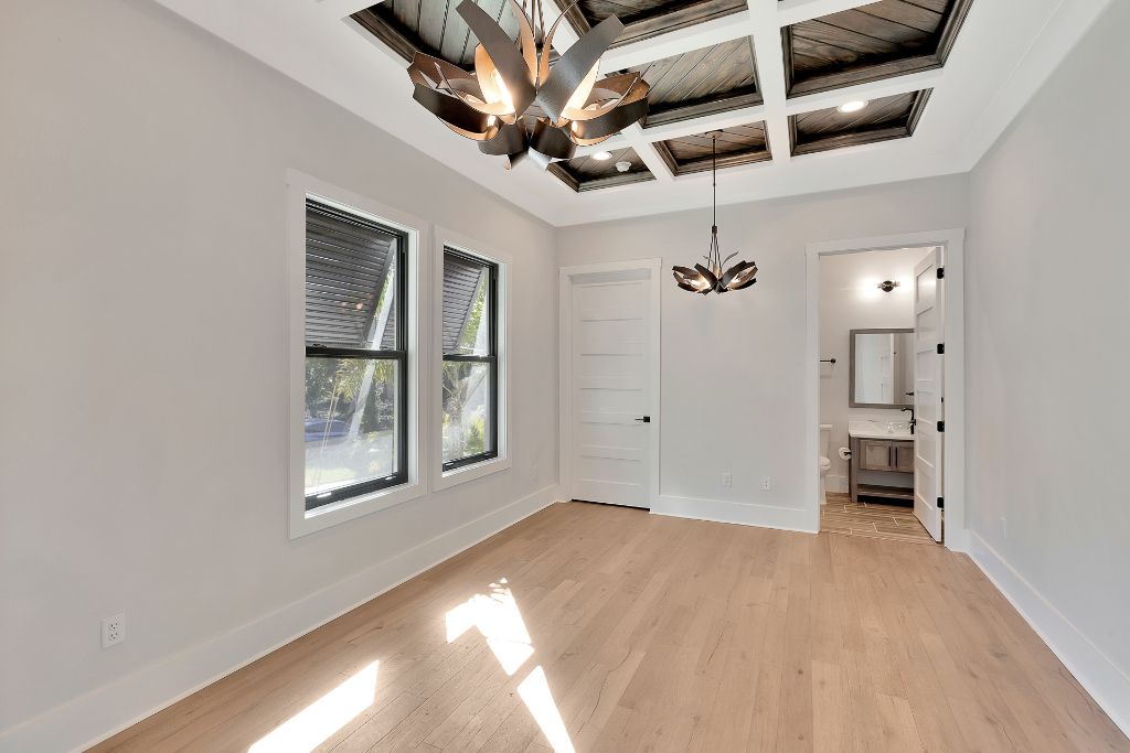 Sun-drenched bedroom suite with dark coffered ceiling, sculptural botanical chandelier and ensuite bathroom