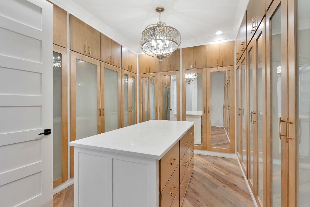 Custom luxury walk-in closet with floor-to-ceiling maple cabinetry, glass doors, quartz island and chandelier