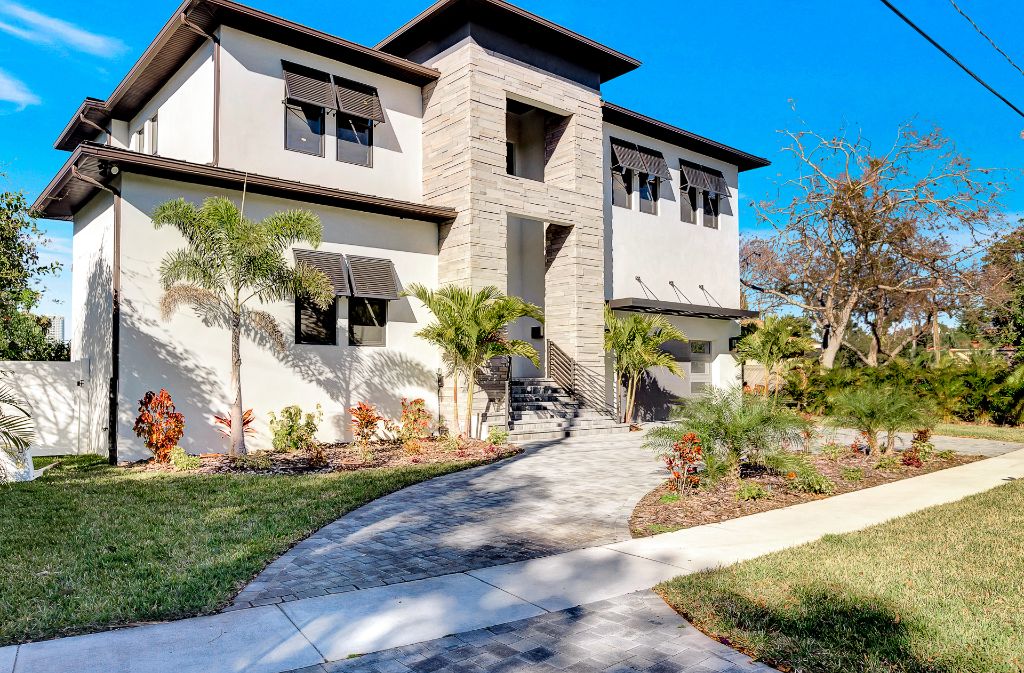 Modern two-story Tampa home with stone tower, louvered shutters, paver driveway and tropical landscaping