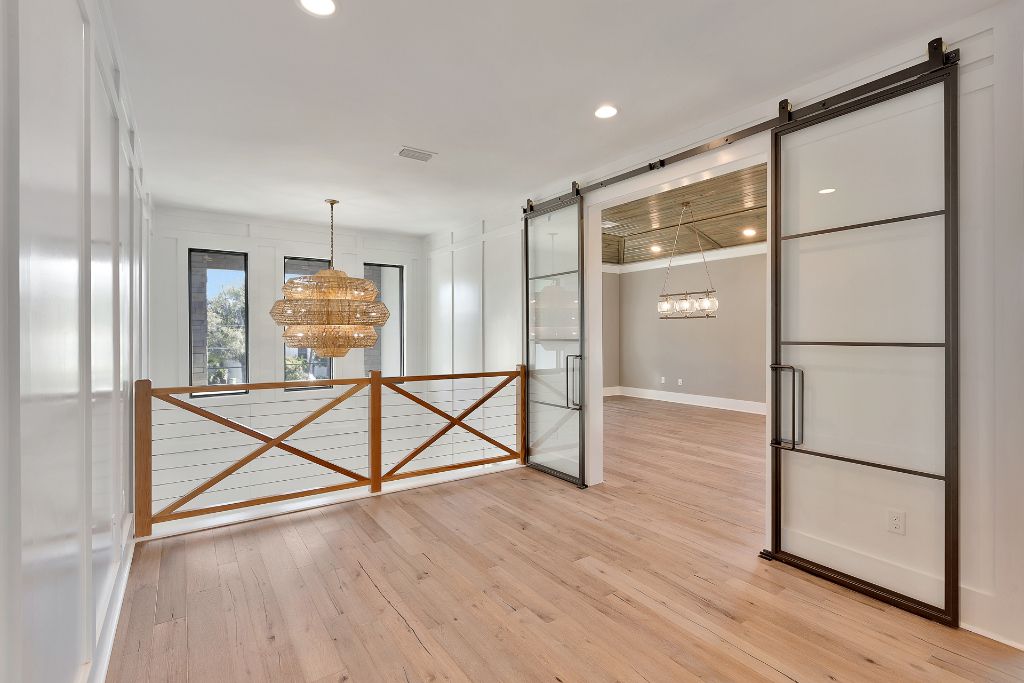 Airy hallway landing with steel barn door, shiplap paneling, woven pendant light and natural wood railing