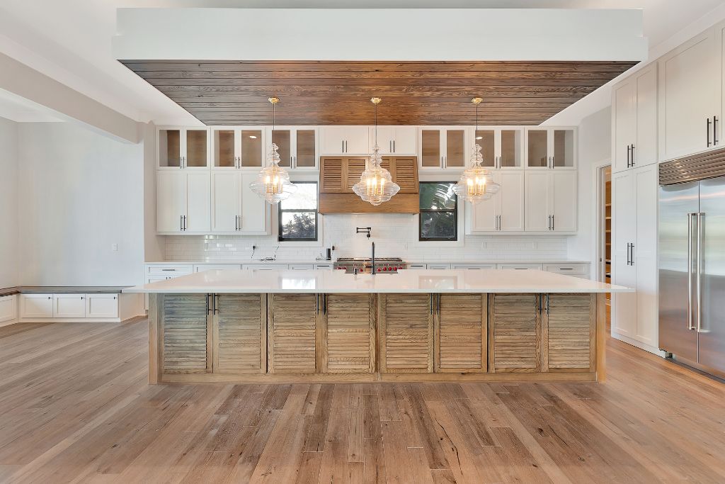 Open kitchen with shutter-panel island, wood ceiling tray, glass pendants, white cabinetry and stainless appliances